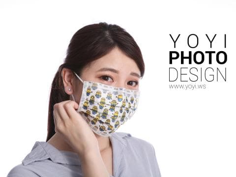 這張「戴著印有小小兵圖案口罩的女性」的照片是，一位年輕女性戴著印有小小兵圖案的口罩，用手輕輕地扶著口罩，露出溫柔的笑容。