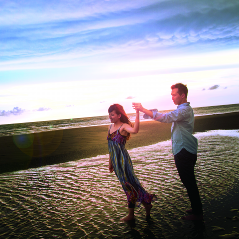 這張照片是一對男女在海邊牽手散步，夕陽餘暉灑落在他們身上，展現出浪漫的氛圍。