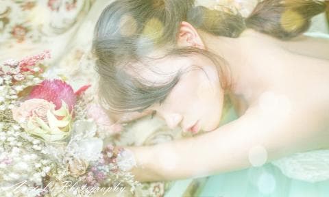 這張「一位女性在花叢中睡覺」的照片是，她閉著眼睛，頭髮散落在臉上，身上穿著白色的蕾絲服裝，背景是一片朦朧的花海。