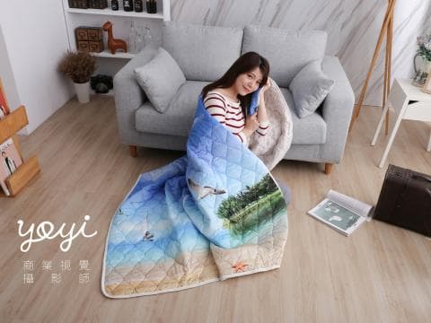 這張照片是一個年輕女子坐在沙發上，蓋著印有海洋圖案的毯子，看起來很舒服。