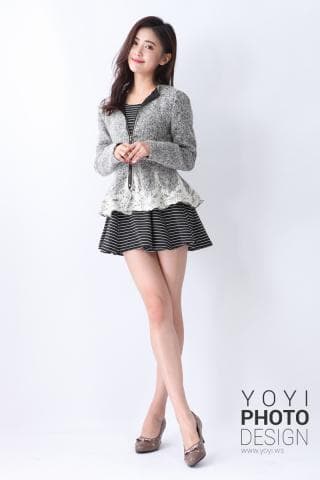 這張照片是一位年輕女性，她穿著一件灰色的夾克和一條黑白條紋的裙子，並搭配一雙棕色的高跟鞋，她微笑著看著鏡頭。