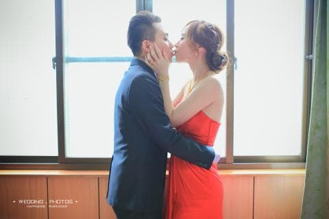 這張照片是一對情侶正在擁吻，他們看起來很甜蜜，背景是一扇窗戶，窗外是陽光灑落的景色。