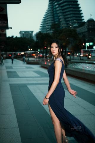 這張照片是一個穿著藍色禮服的女孩站在都市中，她的背景是一棟現代的建築。她看起來很優雅，並且充滿自信。