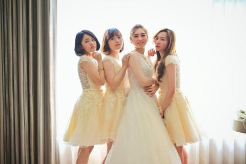 這張照片是四個女孩的婚禮照，其中一個女孩穿著白色婚紗，其他的女孩則穿著淺黃色的禮服，她們都笑容滿面，看起來非常幸福。
