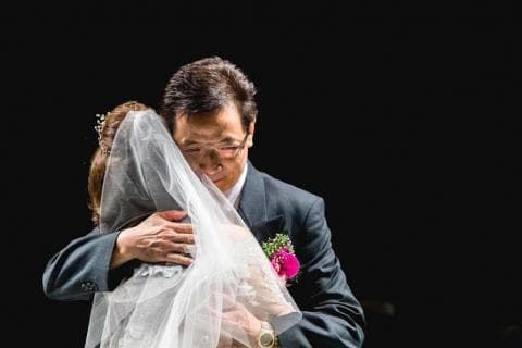 這張照片是父親緊緊擁抱著即將出嫁的女兒，他滿臉愛意，眼中泛著淚光，女兒則依偎在他的懷裡，表現出對父親的不捨與愛。