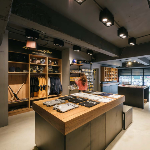 這張「棒球用品店」的照片是一個現代化的商店，裡面有許多棒球相關商品，例如球衣、帽子和球棒。商店也有一名女性顧客正在選購商品。