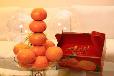 這張照片是一堆橘子放在一個紅色的橘子禮盒上，橘子堆成金字塔狀，看起來很美味。