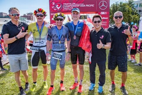 這張照片是五位參加鐵人三項賽的運動員。他們都穿著運動服，並配戴著比賽號碼。他們看起來很健康，並且充滿活力。他們很明顯地為比賽做好了充分的準備。