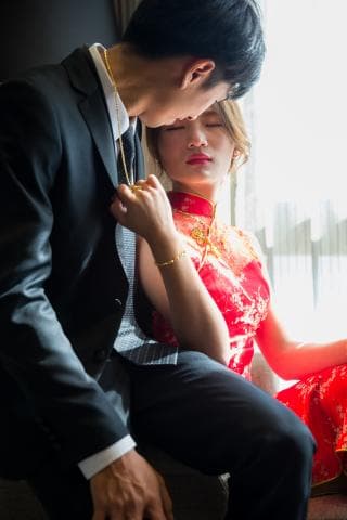 這張照片是一對男女在婚禮上親密互動，男士身穿黑色西裝，女士則穿著紅色旗袍，兩人看起來非常幸福。