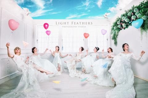 這張照片是六位身穿白色禮服的女性，她們站在一個佈置精緻的攝影棚裡，背景有許多氣球和裝飾，充滿幸福浪漫的氛圍。