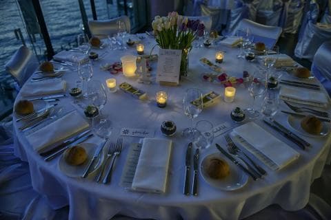 這張照片是一張精緻的餐桌，上面擺滿了餐具、餐盤、餐巾和鮮花，展現了優雅的用餐氛圍。餐桌上的擺設和餐巾的摺疊都非常講究，顯得特別高雅。