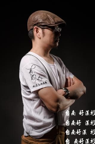 這張照片是一個戴著帽子、穿著白色襯衫的男性，他將手臂交叉放在胸前，看起來很酷。