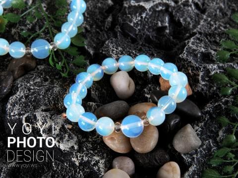 這張照片是一條由白色寶石串成的項鍊，它放在一塊石頭上，周圍有許多小石頭。