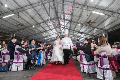 這張照片是新郎新娘在紅色的地毯上，準備進入婚禮會場。他們都穿著傳統的婚禮服裝，新郎穿著西裝，新娘穿著婚紗。他們的手上都拿著花束，看起來非常幸福。