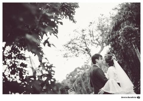 這張照片是一對新人正在樹林裡擁吻。新郎穿著西裝，新娘穿著婚紗，他們深情地看著彼此，看起來非常幸福。