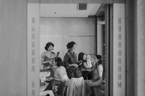 這張照片是四個女性在化妝間裡準備婚禮，其中一個穿著婚紗，其他的女性正在幫她化妝。她們的臉上都洋溢著幸福的笑容，讓人感受到她們對婚禮的期待和喜悅。