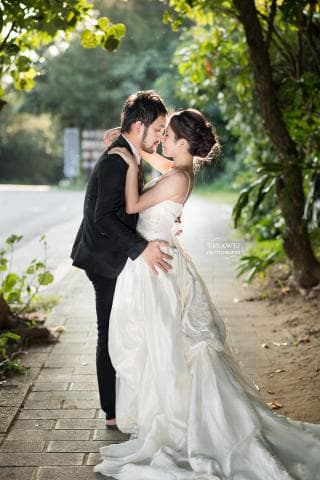 這張照片是一對新人在戶外拍婚紗照，最重要的是他們互相依偎著，新娘身穿白色婚紗，新郎則穿著黑色西裝，他們彼此深情凝望，甜蜜幸福，畫面充滿浪漫的氛圍。