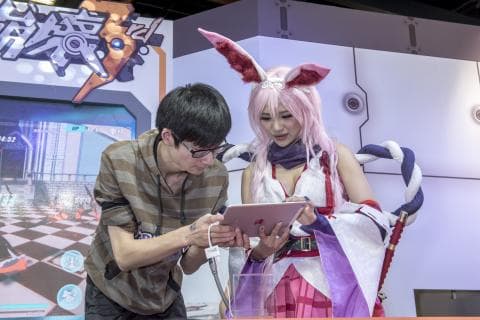 這張「遊戲展」的照片是一個年輕男子和一個穿著動漫服裝的年輕女子。男子正在看平板電腦，女子則在看著男子。