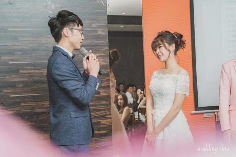 這張婚禮的照片是一對新人正在進行婚禮儀式。新郎手拿麥克風，新郎則穿著白色婚紗，看起來很幸福。