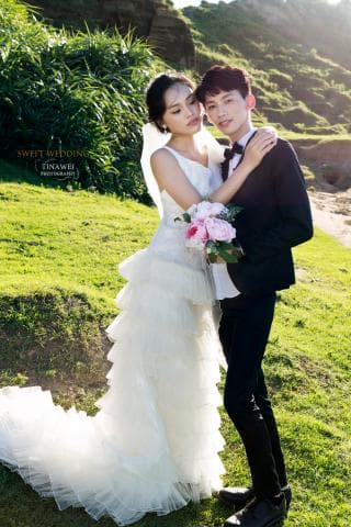 這張照片是一對新人在戶外拍攝婚紗照，照片中最重要的部分是新郎新娘互相依偎，新郎的手環抱住新娘的腰，新娘則將手放在新郎的胸口，他們臉上洋溢著幸福的笑容，畫面溫馨甜蜜。