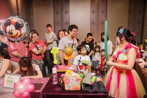 這張「慶祝派對」的照片是小朋友在舞臺上玩耍，氣球和小丑表演很熱鬧，旁邊有許多大人在觀看。