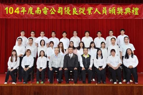 這張照片是104年度南電公司優良從業人員頒獎典禮，照片中包含許多員工，他們站在舞臺上，並排站成兩排，穿著白色襯衫和黑色西裝褲，以及領帶。