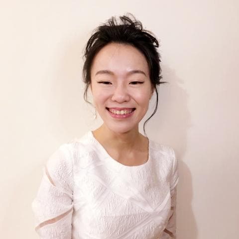 這張「一位女性」的照片是，她穿著白色蕾絲洋裝，頭髮盤起來，露出甜美的笑容。