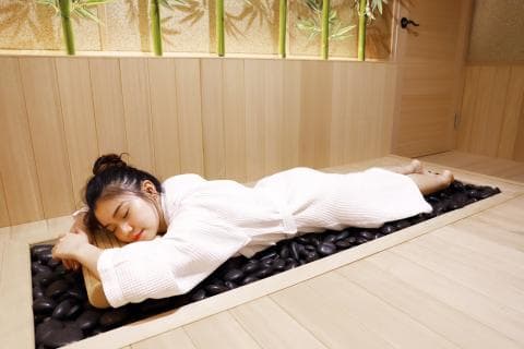 這張照片是一名女子在木地板上睡在石頭上，她穿著白色浴袍，看起來很放鬆。