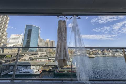 這張照片是一件美麗的婚紗和頭紗，掛在陽臺的欄杆上。婚紗是蕾絲做的，頭紗是薄紗的，它們在陽光下閃閃發光，十分漂亮。