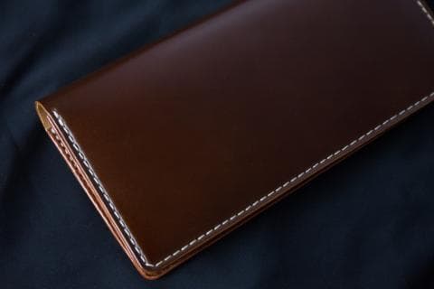 這張照片是一個皮革錢包。錢包是深棕色，並有白色縫線。錢包的皮革表面光滑且有光澤。