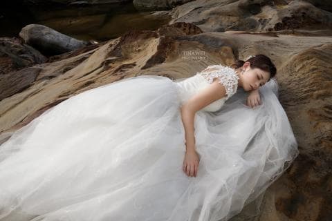 這張「婚紗照」的照片是一個新娘，穿著白色婚紗，躺在石頭上。