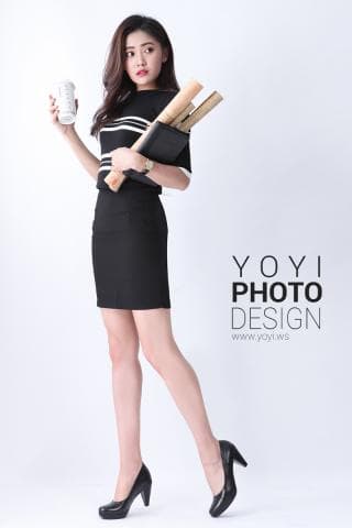 這張「時尚女性」的照片是一名穿著黑色短裙和白色條紋上衣的年輕女子，她手裡拿著一本筆記本和幾根捲尺，她站在一個白色的背景前，看起來很有自信和專業。