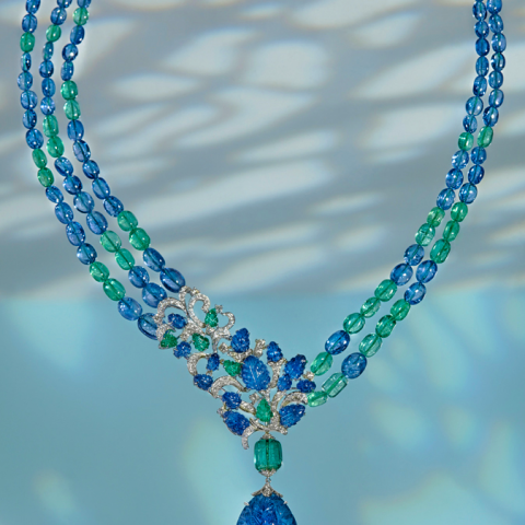 這張照片是一個由藍寶石和祖母綠珠子串成的項鍊，中間有一個精緻的藍寶石吊墜，上面鑲嵌著鑽石，設計成花朵的形狀，非常華麗。