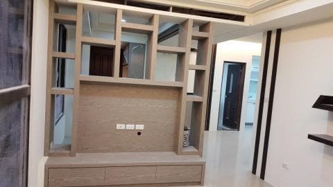 這張照片是一個現代化的客廳，其中最顯眼的部分是一個木質的電視櫃，上面裝有層架，下方有抽屜。電視櫃的設計簡約，但很有質感，搭配周圍的白色牆壁和地板，營造出舒適而現代的氛圍。