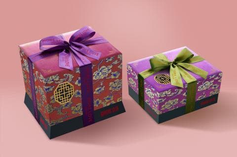 這張照片是兩個禮物盒，一個大一個小，都用華麗的傳統中國圖案裝飾，並綁著緞帶。  盒子上的圖案以紅色和紫色為主，並帶有金色花紋和字體，散發出高貴典雅的氣息。