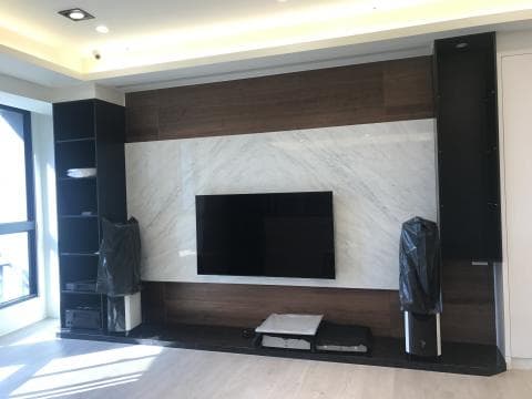 這張照片是一間客廳的電視牆，牆面採用大理石做裝飾，電視牆上有一台電視和音響，牆面看起來很高級。