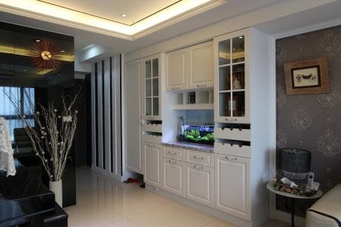 這張照片是一個現代化的廚房，裡面的櫥櫃是白色的，上面有玻璃門，裡面的酒杯架裝飾著閃亮的酒杯，看起來很漂亮。