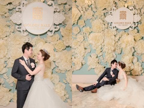 這張照片是一對新人在一個佈滿白色花朵的牆壁前拍攝婚紗照。新郎穿著黑色西裝，新娘穿著白色婚紗，他們深情地對望著對方，看起來幸福美滿。