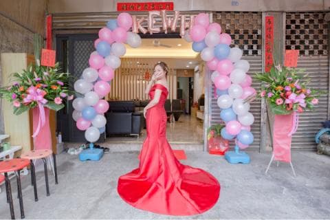 這張「婚禮」的照片是一個穿著紅色禮服的新娘，站在由氣球組成的拱門前，並擺出一個可愛的姿勢。