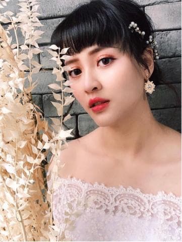 這張「婚紗照」的照片是一位美麗的新娘，她穿著白色蕾絲婚紗，頭上戴著珍珠髮飾，耳朵上則戴著精緻的耳環，露出甜蜜的笑容，背景是一片灰色的磚牆和一束白色的乾燥花，整體畫面充滿幸福和浪漫的氛圍。