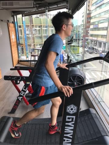 這張照片是一個男人在使用健身器材跑步。 他正踏上跑步機，並握住扶手。 他的動作看起來十分專注。