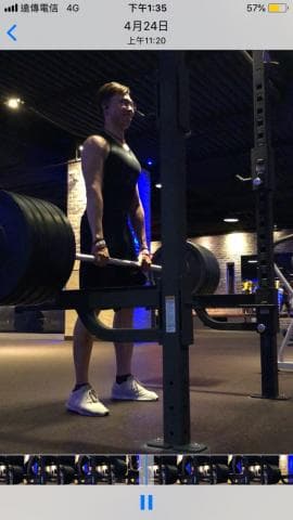 這張照片是一個男人在健身房舉重。他正準備從地面上舉起一個槓鈴。他正在使用一個槓鈴架來幫助他舉起重量。