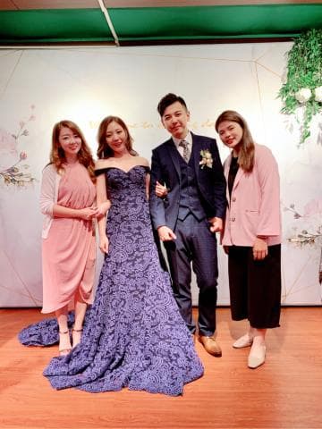 這張「婚禮」的照片是一對新人和兩位朋友在婚禮現場的合照。 新娘穿著紫色蕾絲禮服，新郎穿著深色西裝，兩位朋友都穿著粉紅色服裝。