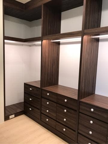 這張照片是一間房間裡面的衣櫥，衣櫥的門是開著的，可以看到裡面有許多抽屜和層架。抽屜的材質是木頭的，顏色是深棕色，看起來很高級。