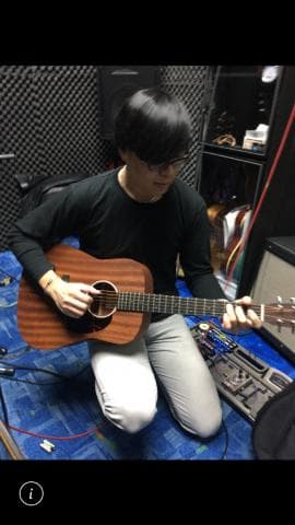 這張照片是一名男子坐在錄音室裡彈著一把木吉他。