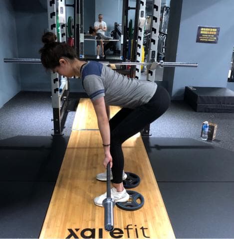 這張照片是一個女性在健身房舉重，她正準備用槓鈴舉重。她正彎下腰，雙手緊緊抓住槓鈴，準備抬起來。