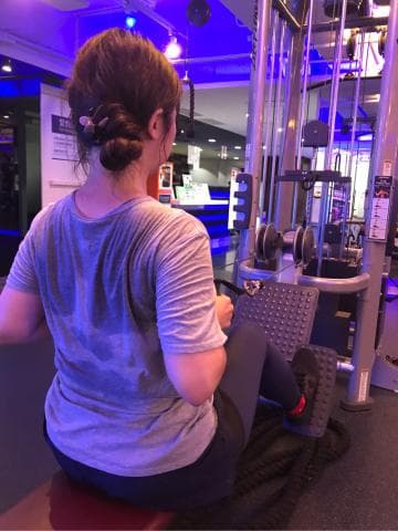 這張照片是一個女性正在健身房使用器材運動，她的汗水沾濕了衣服，展現出努力運動的狀態。