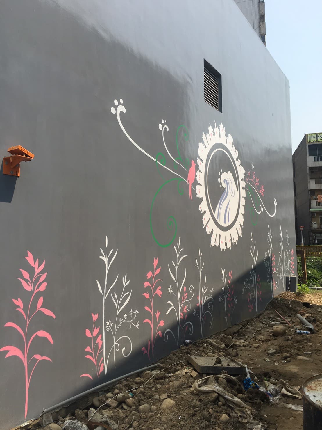 這張「牆壁塗鴉」的照片是，上面畫著一個圓形圖案，裡面有一隻鳥和一個海浪的圖案，周圍還有很多植物。