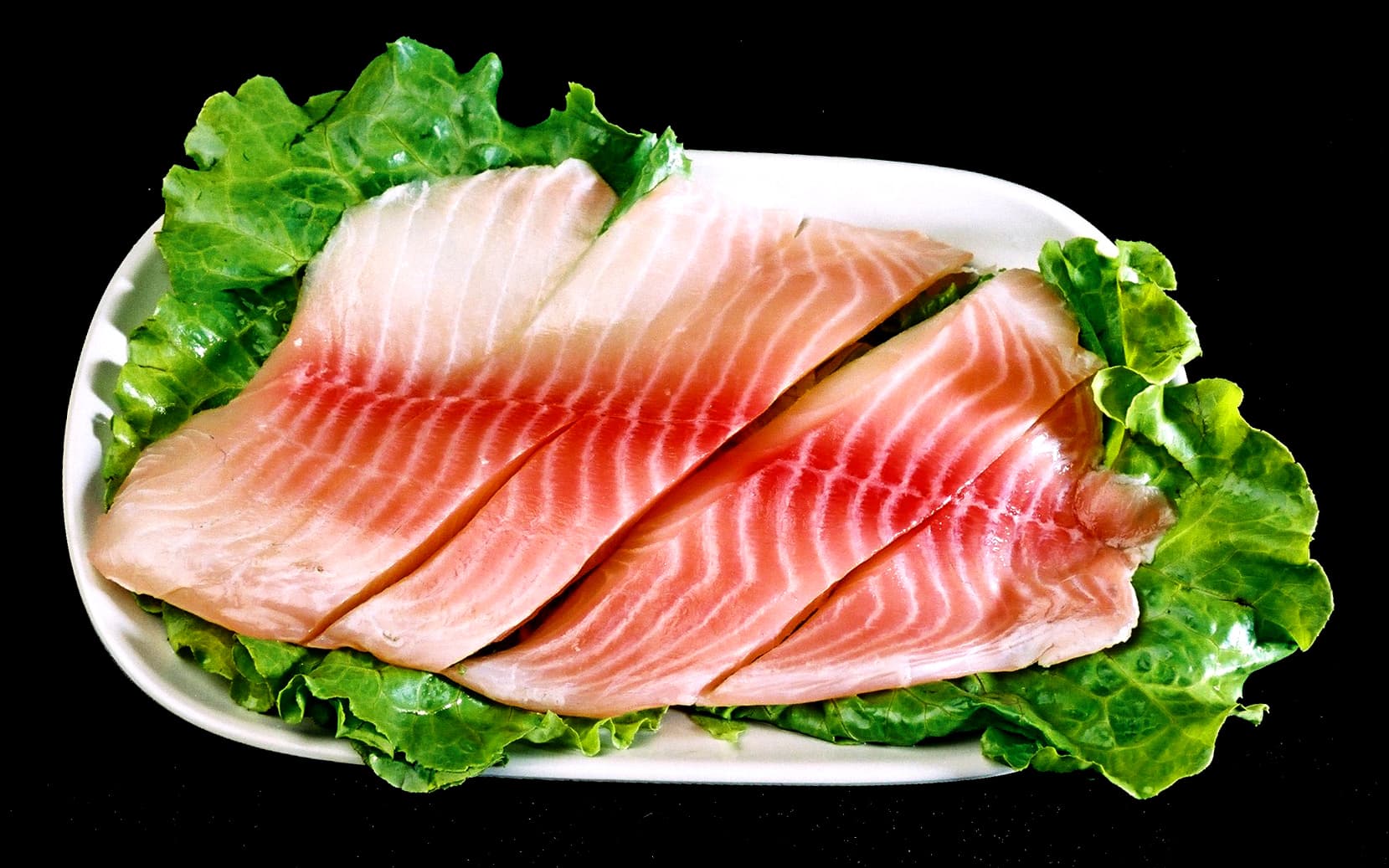 這張「生魚片」的照片是一盤擺在綠色生菜上的魚片。魚片是白色的，帶有紅色條紋。