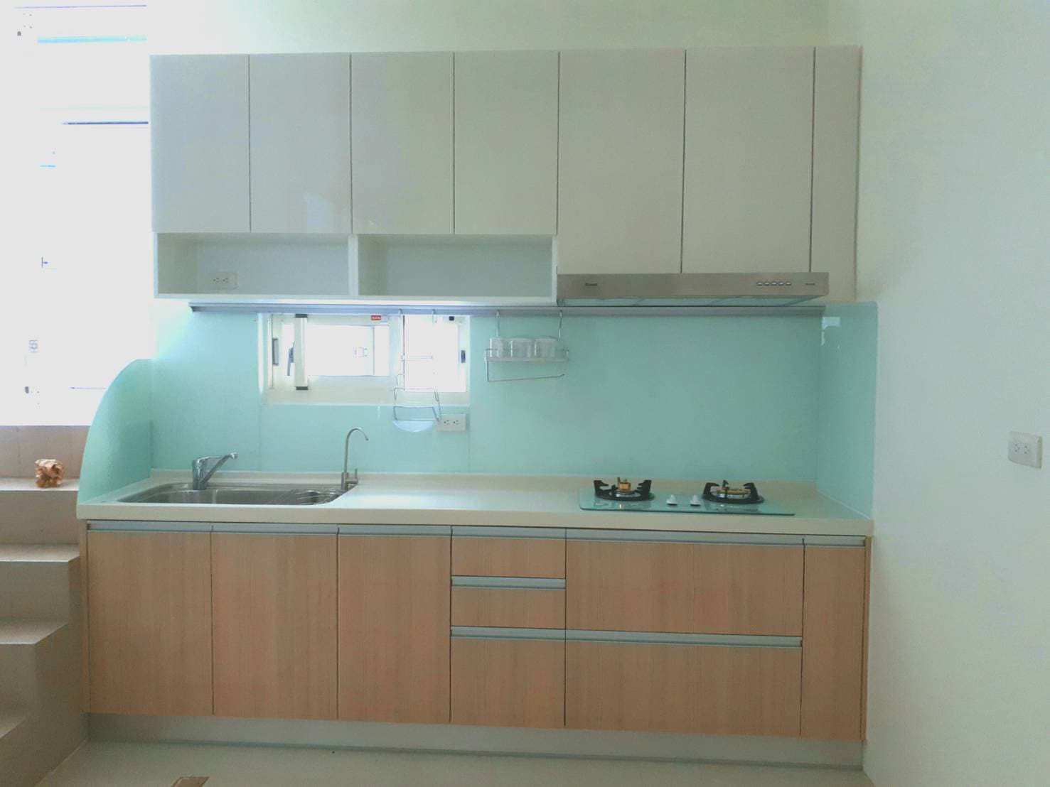 這張照片是一個現代化的廚房，其中最重要的是淡綠色的牆面，上面裝有白色櫥櫃和一個抽油煙機。 牆面和櫥櫃的顏色搭配得很好，看起來非常乾淨簡潔。